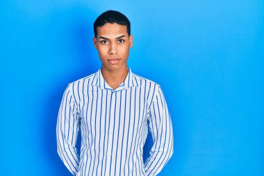 Gündelik kıyafetler giyen genç Afro-Amerikalı adam yüzünde ciddi bir ifadeyle rahatlamış. Basit ve doğal bir şekilde kameraya bakıyorsun.. 