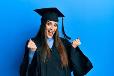 Mezuniyet şapkası ve tören cübbesi giyen güzel esmer kadın kollarını kaldırarak ve açık gözlerle başarının şaşkınlığını ve şaşkınlığını yaşıyor. Kazanan konsept. 