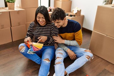 Young latin couple choosing paint color sitting on the floor at new home.
