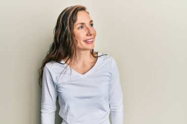 Sıradan kıyafetler giyen genç sarışın kadın yüzünde gülümsemeyle yan yana bakıyor, doğal bir ifade. Kendinden emin gülen. 