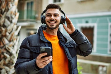 Yakışıklı, sakallı, neşeli, kendine güvenen, kışlık palto giyen, akıllı telefondan müzik dinleyen bir İspanyol.