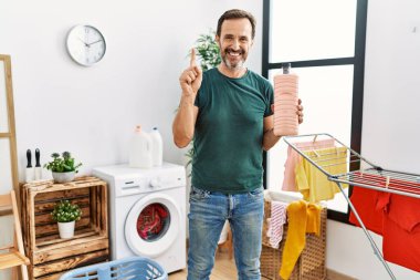 Sakallı orta yaşlı bir adam çamaşır deterjanı şişesini tutarken bir fikir ya da soru işareti ile gülümsüyor. 