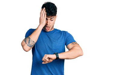 Gündelik tişört giyen genç İspanyol adam saate bakıyor. Endişeli, geç kalmaktan korkuyor. 