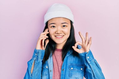 Genç Çinli kız akıllı telefondan konuşuyor parmaklarıyla imza atıyor, gülümsüyor ve mükemmel bir sembol. 