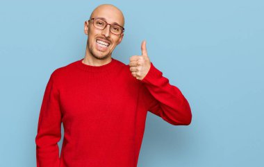 Sakallı, sıradan giyinmiş, gözlüklü, mutlu ve pozitif gülümseyen, başparmağıyla mükemmel ve onay işareti yapan kel bir adam. 