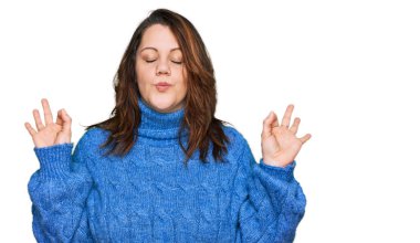 Genç ve cüsseli bir kadın günlük kıyafetler giyiyor rahatlıyor ve gözleri kapalı gülümsüyor parmaklarıyla meditasyon hareketi yapıyor. yoga konsepti. 