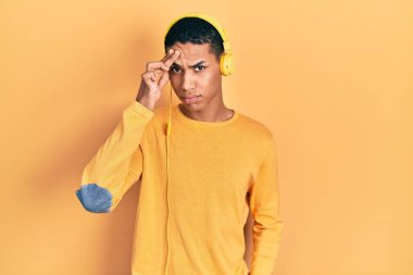 Genç Afro-Amerikalı adam kulaklık takarak müzik dinliyor. Alnındaki sivilceden mutsuz, siyah noktalı çirkin bir enfeksiyon taşıyor. sivilce ve deri problemi 