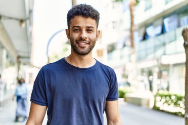 Genç Arap adam, güneşli bir günde kendine güvenerek gülümsüyor.