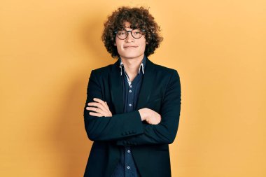 İş ceketi ve gözlük takan yakışıklı genç adam kameraya bakarken kollarını kavuşturup gülümsüyor. pozitif kişi. 