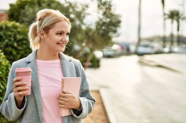 Genç sarışın iş kadını gülümseyerek şehirde kahve içiyor..