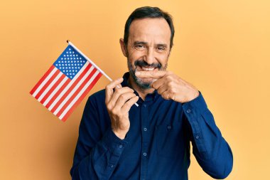 Orta yaşlı, Birleşik Devletler bayrağını tutan İspanyol adam mutlu bir şekilde el ve parmağıyla işaret ediyor. 
