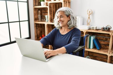 Evde tekerlekli sandalyede oturan orta yaşlı, gri saçlı, engelli bir kadın..
