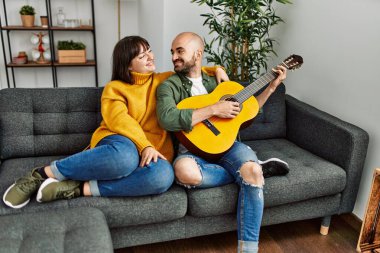 Genç İspanyol çift gülümseyerek evde kanepede oturmuş klasik gitar çalıyor..