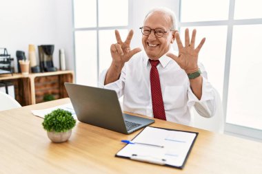 Ofiste çalışan kıdemli bir adam bilgisayarla 8 numarayı gösterip işaret ederken kendinden emin ve mutlu bir şekilde gülümsüyor.. 