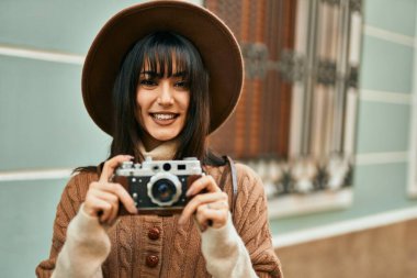 Kışlık şapkalı esmer kadın şehrin dışında klasik kamera kullanarak gülümsüyor.