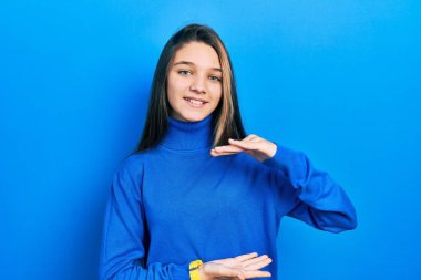 Balıkçı yaka kazak giyen genç esmer kız. Elleri büyük ve büyük bir işaret, ölçü sembolü gösteriyor. Kameraya bakıp gülümsüyor. ölçüm kavramı. 