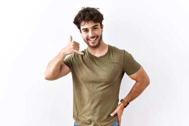 İspanyol bir adam izole edilmiş beyaz arka planda durup gülümsüyor telefonla el ve parmaklarıyla telefonla konuşuyor gibi yapıyor. iletişim kavramları. 