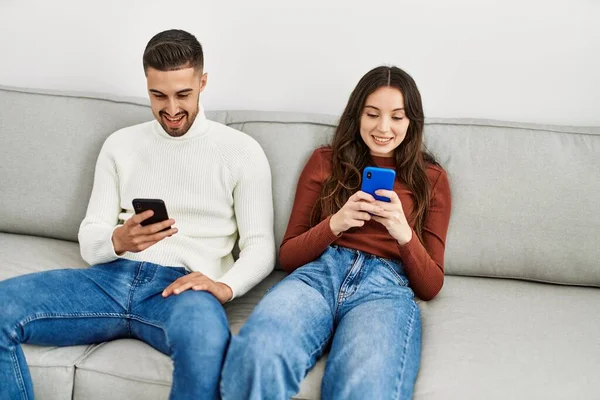 Evdeki Kanepede Oturan Akıllı Telefon Kullanan Genç Spanyol Çift — Stok fotoğraf
