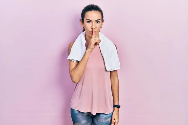 Young brunette woman wearing sportswear and towel asking to be quiet with finger on lips. silence and secret concept.