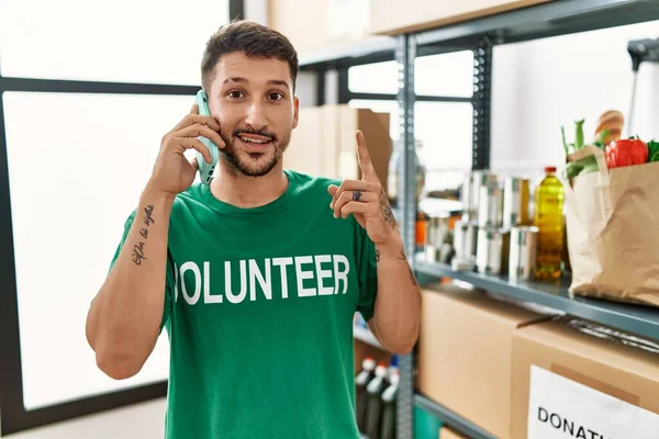 Joven Hombre Hispano Con Camiseta Voluntaria Hablando Por Teléfono Sorprendido — Foto de Stock