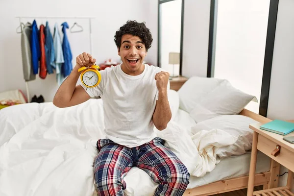 Jovem Hispânico Segurando Despertador Sentado Quarto Gritando Orgulhoso Celebrando Vitória — Fotografia de Stock