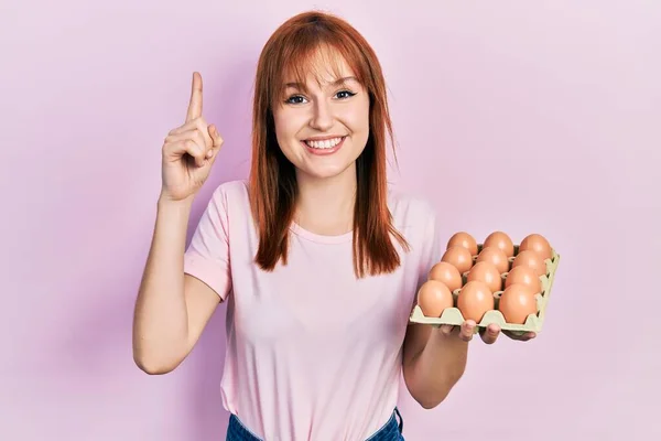 Руда Молода Жінка Показує Свіжі Яйця Посміхаючись Ідеєю Або Питанням — стокове фото