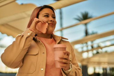 Genç İspanyol kız akıllı telefondan konuşuyor ve şehirde kahve içiyor..