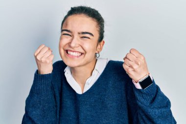 Gündelik kıyafetler giyen, mutlu ve heyecanlı genç beyaz bir kız kolları havada, gülümseyen ve başarı için bağıran, kazanan bir jest yapıyor. kutlama konsepti. 