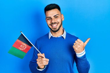 Sakallı, Afgan bayrağı taşıyan, ağzı açık gülümseyen genç İspanyol bir adam. 