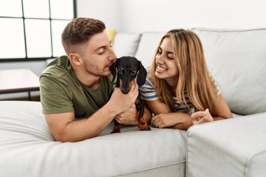 Genç İspanyol çift köpeği öpüyor ve evdeki kanepede uzanıyor..