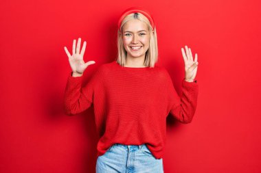 Güzel sarışın kadın gündelik kırmızı süveter giyer ve dokuz numarayı göstererek gülümserken kendinden emin ve mutlu.. 