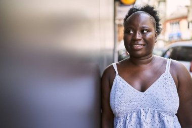 Genç Afrikalı Amerikalı kadın gülümseyerek şehirde mutlu mesut duruyor..