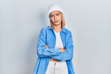 Yün şapka takan, kuşkucu ve gergin güzel sarışın bir kadın. Yüzünde çapraz kollu tasvip etmeyen bir ifade. negatif kişi. 