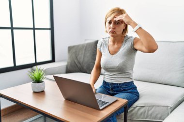 Orta yaşlı sarışın kadın evde dizüstü bilgisayar kullanıyor. Alnındaki sorun yüzünden endişeli ve stresli. Kriz için endişeli. 