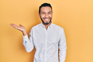 Sakallı, iş gömleği giyen, neşeli bir şekilde gülümseyen ve avuç içi kameraya bakan İspanyol bir adam.. 