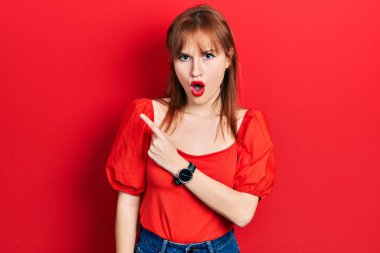 Kırmızı tişörtlü kızıl saçlı genç kadın parmaklarını yana doğru göstererek şaşırdı, ağzı açık hayret içinde kaldı.. 