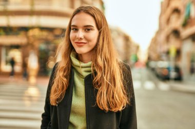 Genç sarışın kız gülümsüyor, mutlu bir şekilde şehirde duruyor..