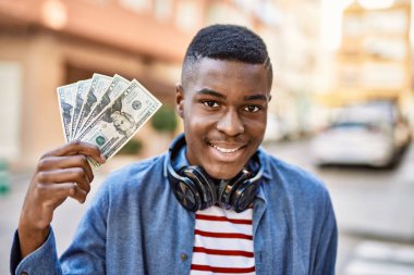 Genç Afrikalı Amerikalı adam şehirde elinde dolarlarla kulaklık takıyor..