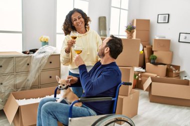 Orta yaşlı İspanyol çift şampanyayla kadeh kaldırıyor. Tekerlekli sandalyede oturan bir adam ve yeni evinde ayakları üzerinde duran bir köpek.