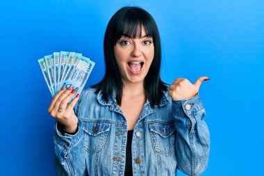 Bangladeş banknotlarını tutan genç İspanyol kadın başparmağıyla işaret ediyor. Ağzını açıp gülümseyerek. 