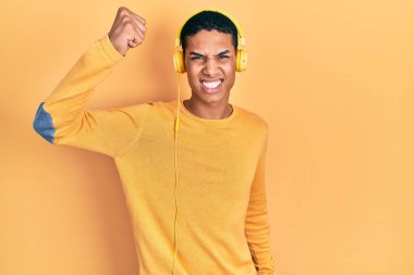 Genç Afro-Amerikalı adam, öfkeli ve kızgın kulaklıklar takarak müzik dinliyor öfkeyle bağırırken sinirli ve öfkeli bir şekilde yumruklarını kaldırıyor. öfke ve agresif konsept. 