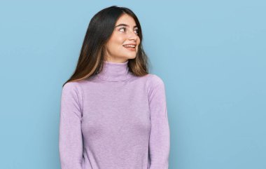 Balıkçı yaka kazak giyen genç ve güzel bir kız yüzünde gülümsemeyle yan yana bakıyor, doğal bir ifade. Kendinden emin gülen. 