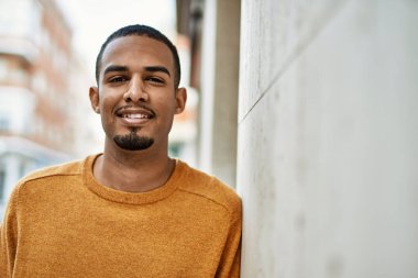 Genç Afrikalı Amerikalı adam gülümseyerek şehirde mutlu mesut duruyor..