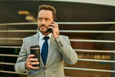 Orta yaşlı işadamı akıllı telefondan konuşuyor ve şehirde kahve içiyor..