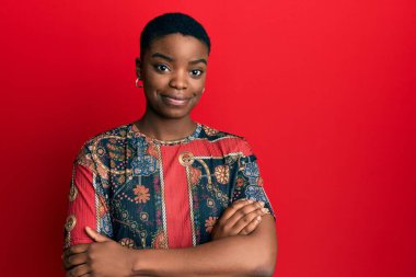 Afrikalı Amerikalı genç bir kadın kollarını kavuşturup kameraya bakarken gülümsüyor. pozitif kişi. 