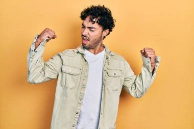 Sıradan kıyafetler giyen genç İspanyol adam gururla gülümseyen kol kaslarını gösteriyor. fitness konsepti. 