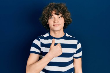 Sıradan çizgili tişört giyen yakışıklı genç adam mutlu bir el hareketi yapıyor. Kameraya bakıp başarıyı gösteren ifade. 