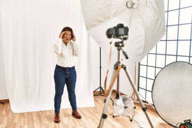 Orta yaşlı İspanyol kadın fotoğraf stüdyosunda mankenlik yapıyor. Acı ve migren yüzünden çaresiz ve stresli bir baş ağrısı çekiyor. Eller başının üstünde.. 