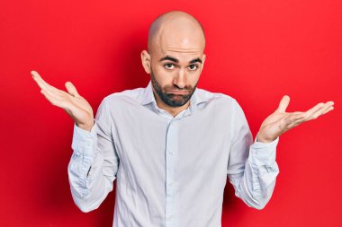 Zarif kıyafetler giyen genç kel adam habersiz ve kolları açık, hiçbir fikri ve şüpheli bir yüzü var.. 