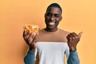 Genç Afro-Amerikalı elinde patates cipsi olan bir adam başparmağını kaldırmış, ağzı açık gülümsüyor. 